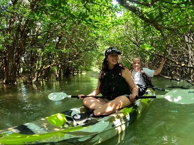 Un hombre y una mujer sonriendo mientras hacen kayak por un denso bosque de manglares