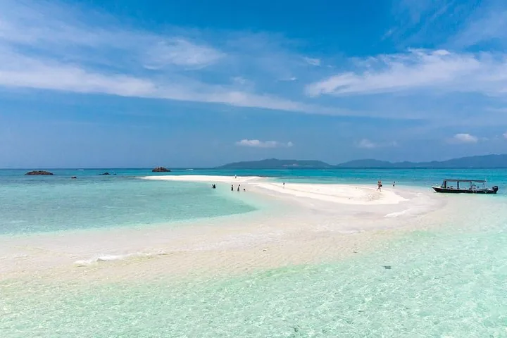 Eine weiße Sandbank, umgeben von türkisfarbenem Wasser, mit einem Boot in der Nähe