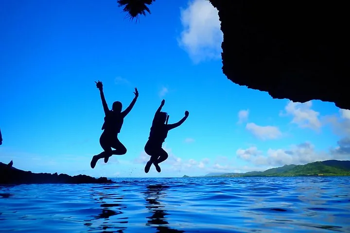 Silhouetten von zwei Personen, die aus einer Felshöhle ins Wasser springen